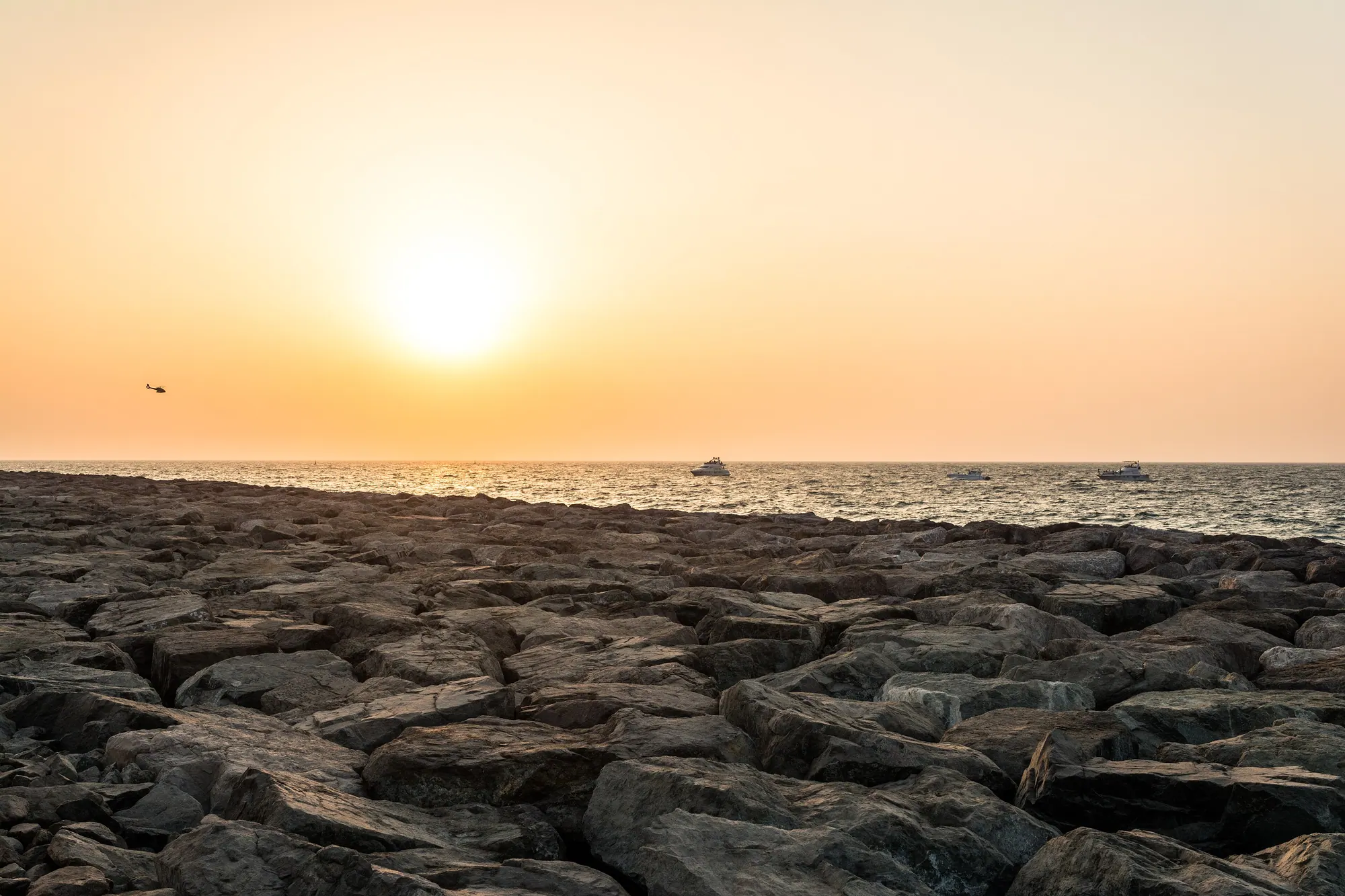 The sun setting over the Arabian Gulf from the rocky shoreline of Palm Jumeirah